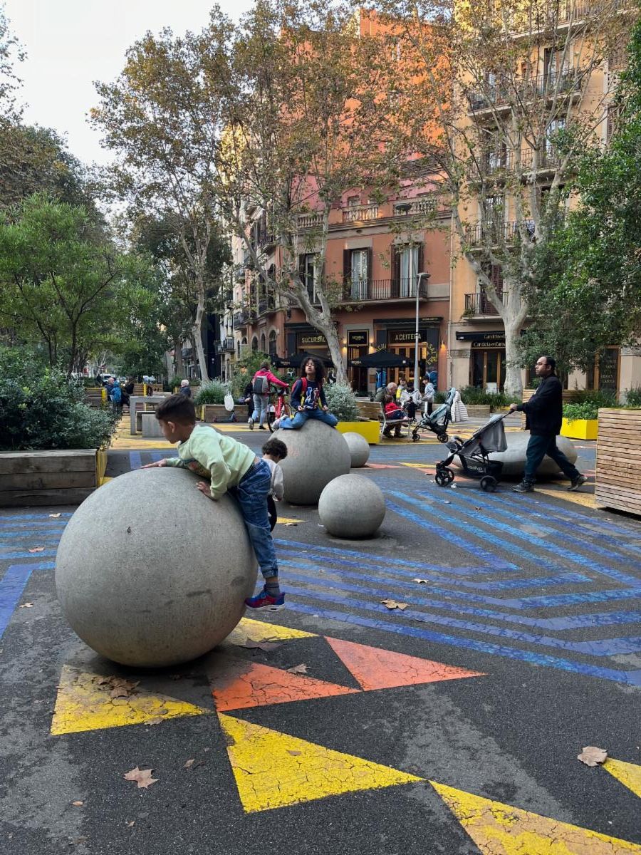 Children playing on concrete sphere bollards in the center of a re-designed intersection.