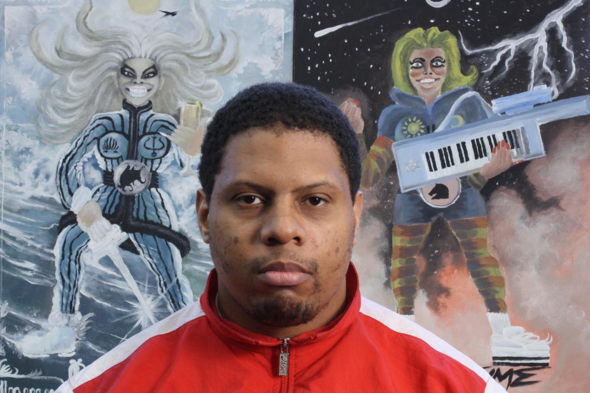 Headshot of Knicoma Frederick in front of 2 pieces of art