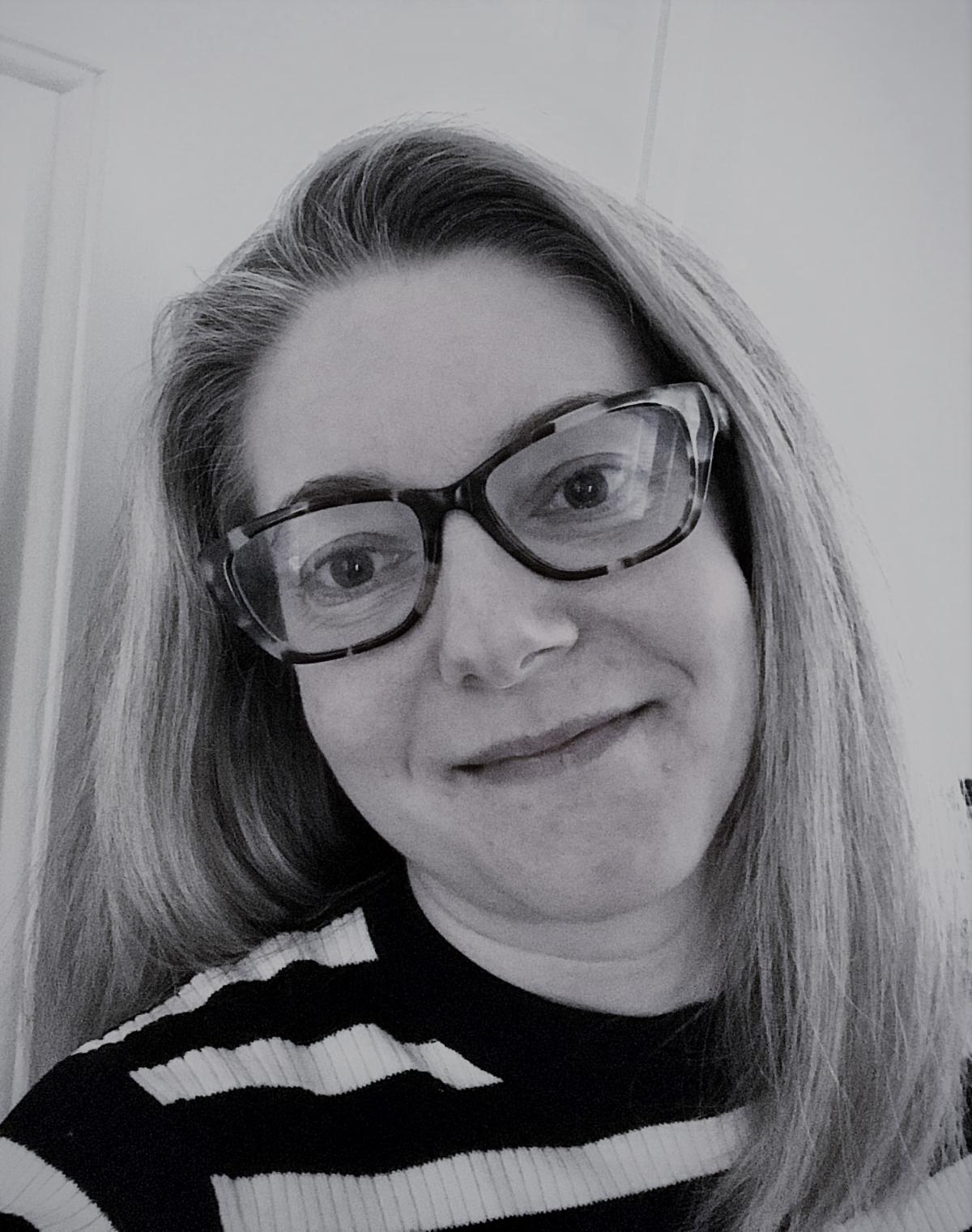Black and white headshot of Kathleen Dinsmore looking straight at camera with her hair down wearing glasses and smiling