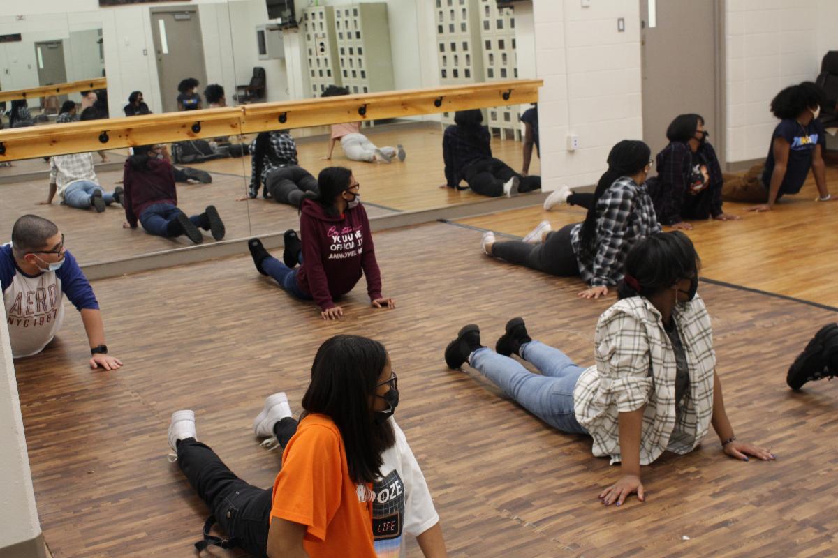 Youth stretching on a wood-patterned floor in front of a mirror in a dance studio