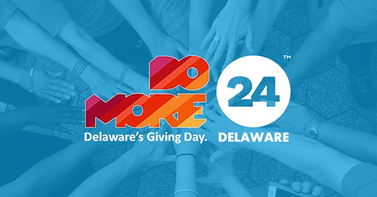 Do More 24 Delaware logo on an image of numerous people reaching their hands into the center of circle to show togetherness that has been given a blue hue Do More 24 Delaware Delaware's Giving Day
