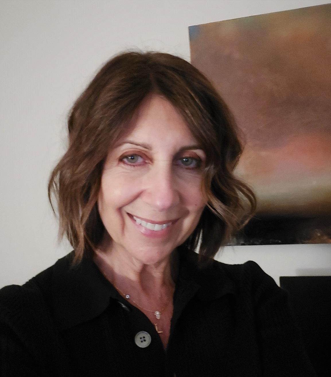 Headshot of Kristin Pleasanton in front of a white wall with a painting hanging on it in the background