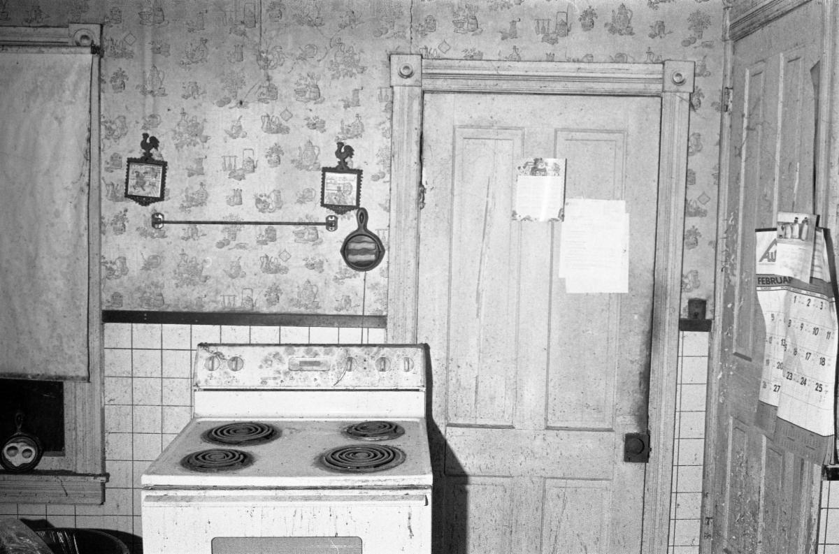 Black and white photograph by Jason Jellick of an old kitchen that does not appear to have been used in a long time with an old electric stove as the focus of the image