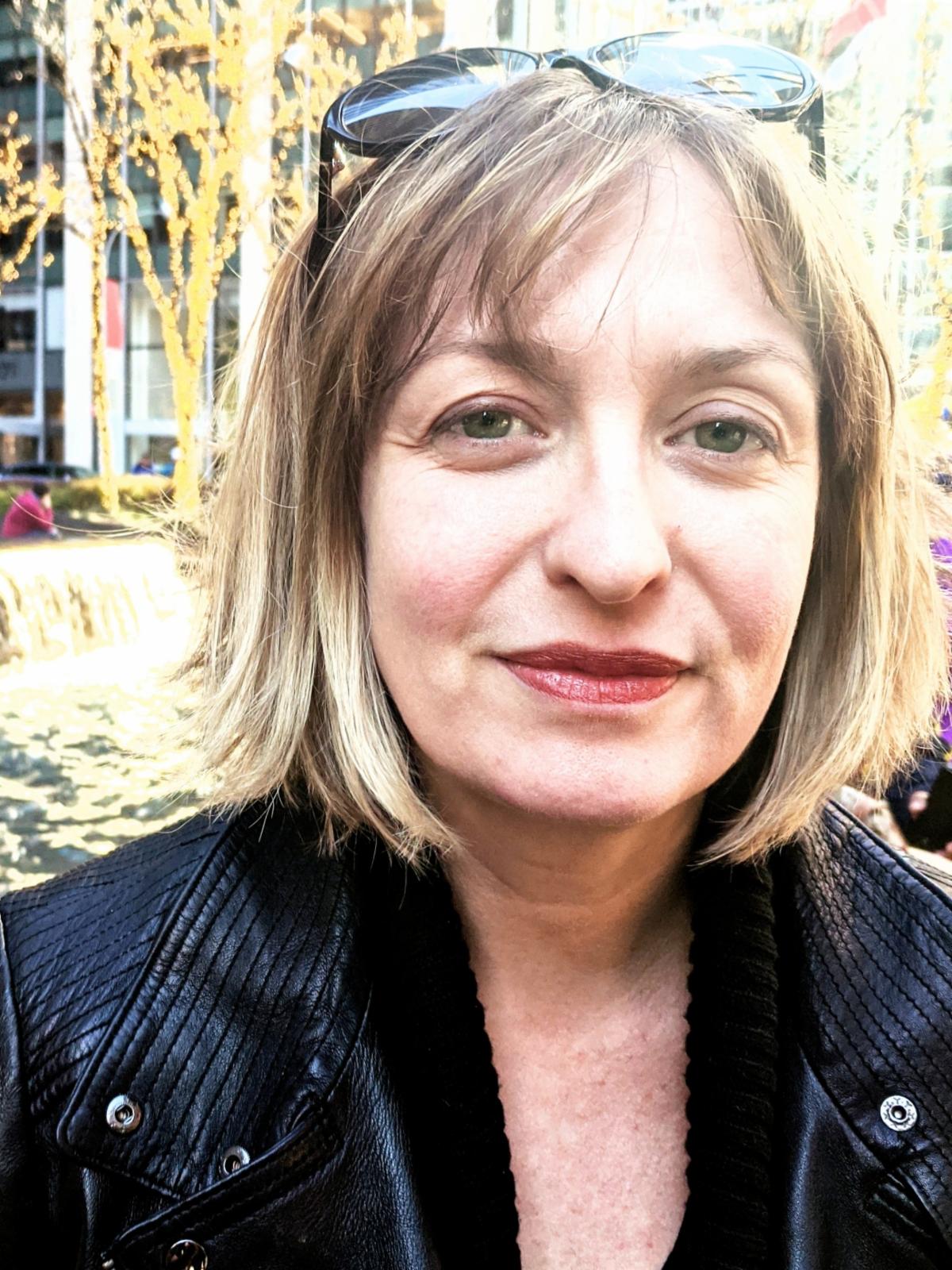 Headshot of Cassandra Lewis outside in front of a water feature surrounded by bare trees completely wrapped in small lights