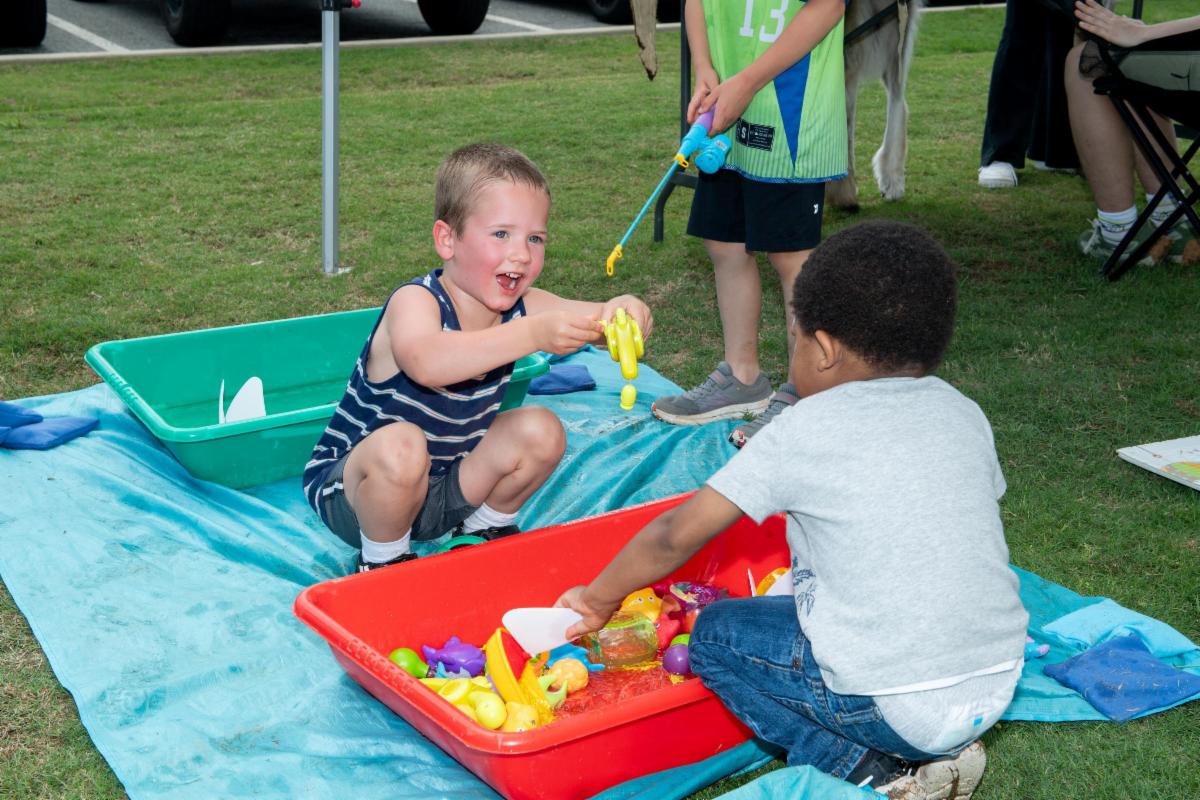 two young kids playing with toys in a small red tub filled with water at the Water Wonders Festival