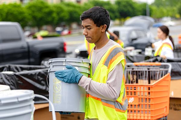 a volunteer at an Earth Day recycling event holding a large paint container