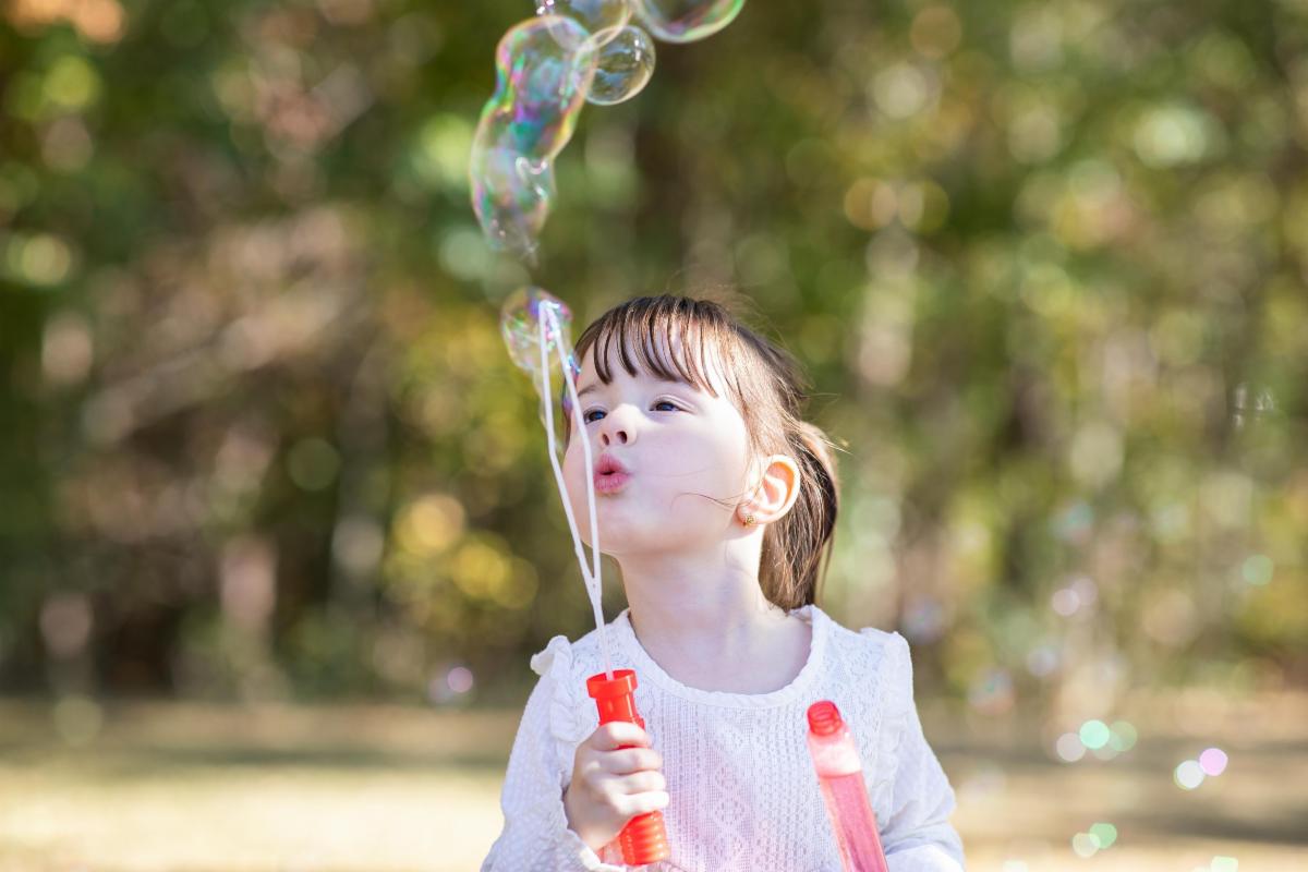 little girl blowing bubbles in a green park
