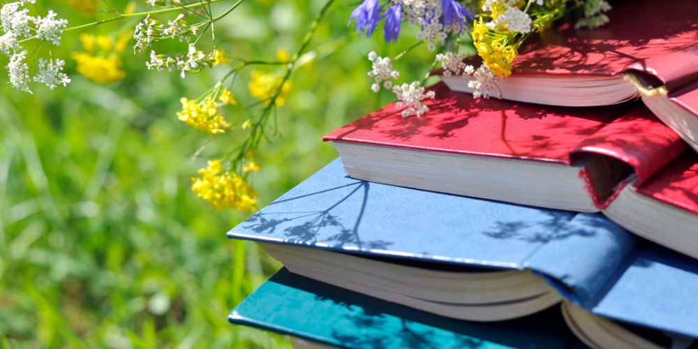 books piled in the grass with wild flowers