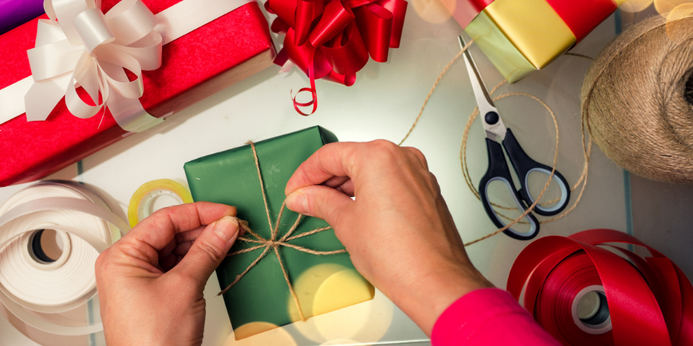 gift wrapping supplies and a person tying a string onto a gift