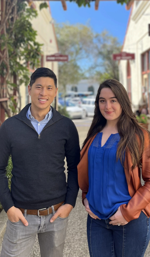 Collaborative team members Garrett Wong and Malia standing together outdoors on a tree-lined street.