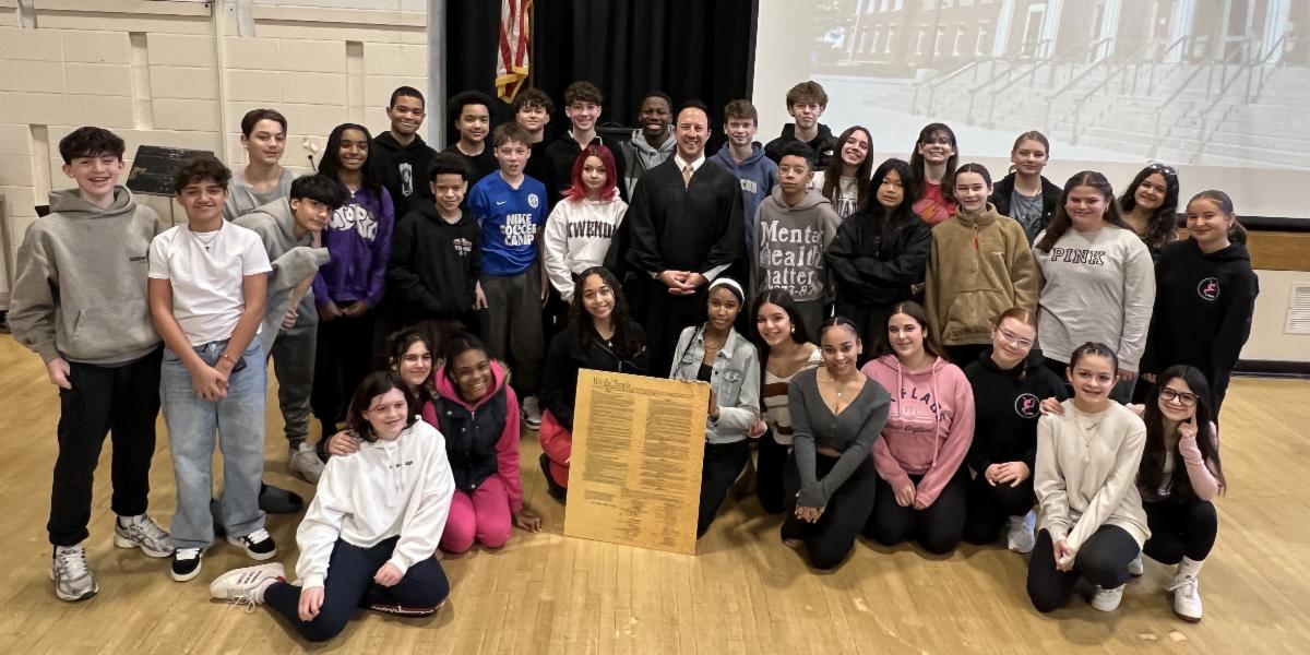 Judge Kaplanes stands for photo with many students in an auditorium/gym.