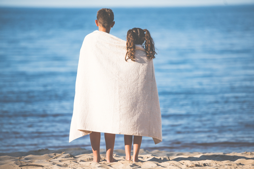 Back view of boy and girl in towel standing together on seashore