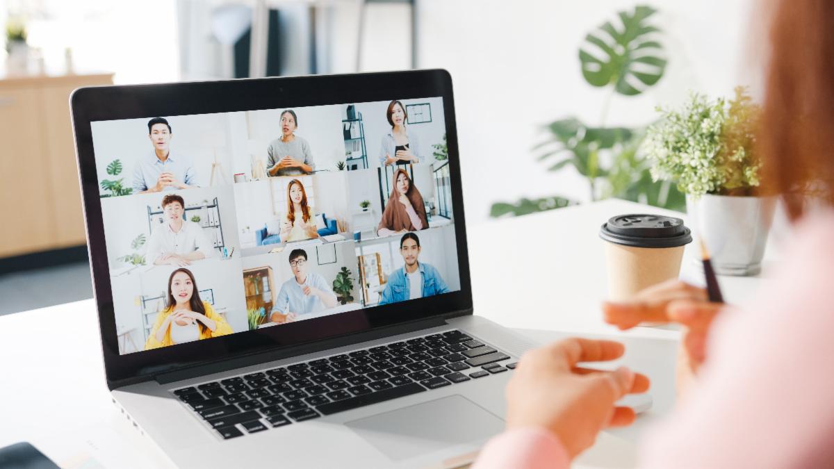 A participant looks at a laptop sitting on a table with virtual meeting members displayed on the screen 