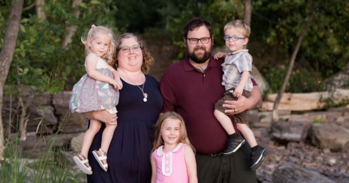 Family of two parents and three children stand on rocks by the lake