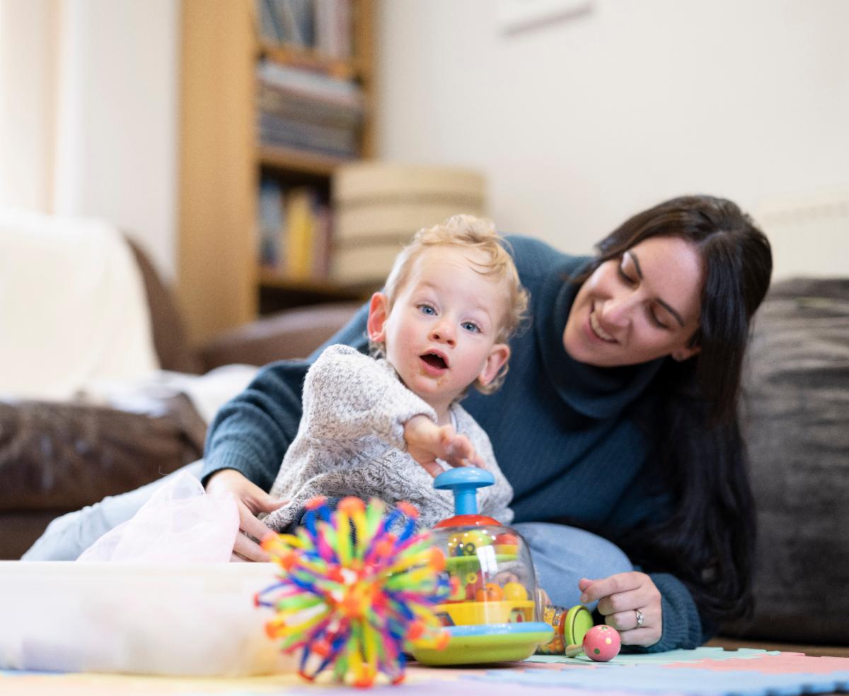 An adult and toddler sit on the floor together while toddler plays with some sensory toys