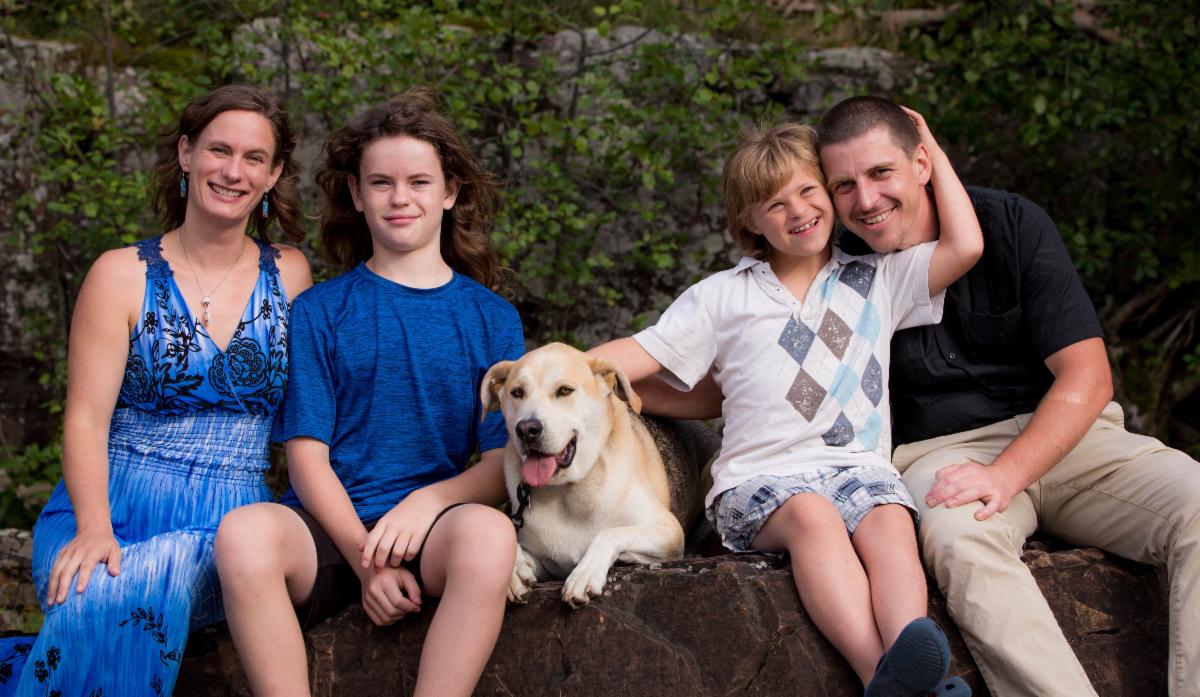 A family including two parents, two children and their dog sit on a large rock