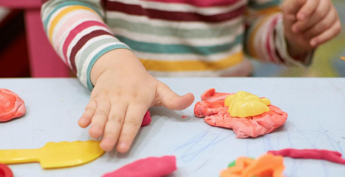 A photo of a childs hands smushing pink and yellow play dough on table