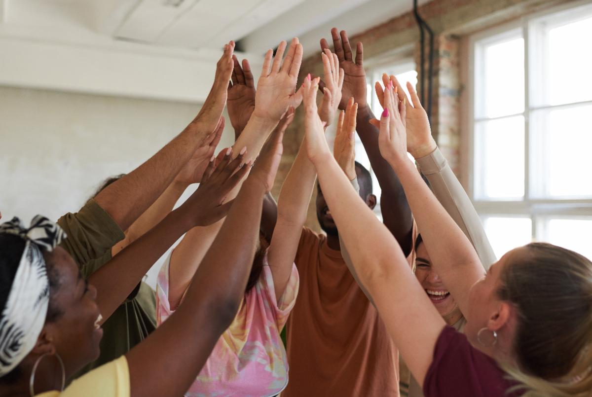 A group of smiling students raise their hands up to meet in the middle of a circle