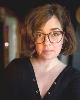 Headshot of Jillian Kirby who wears glasses a and a black v-neck shirt