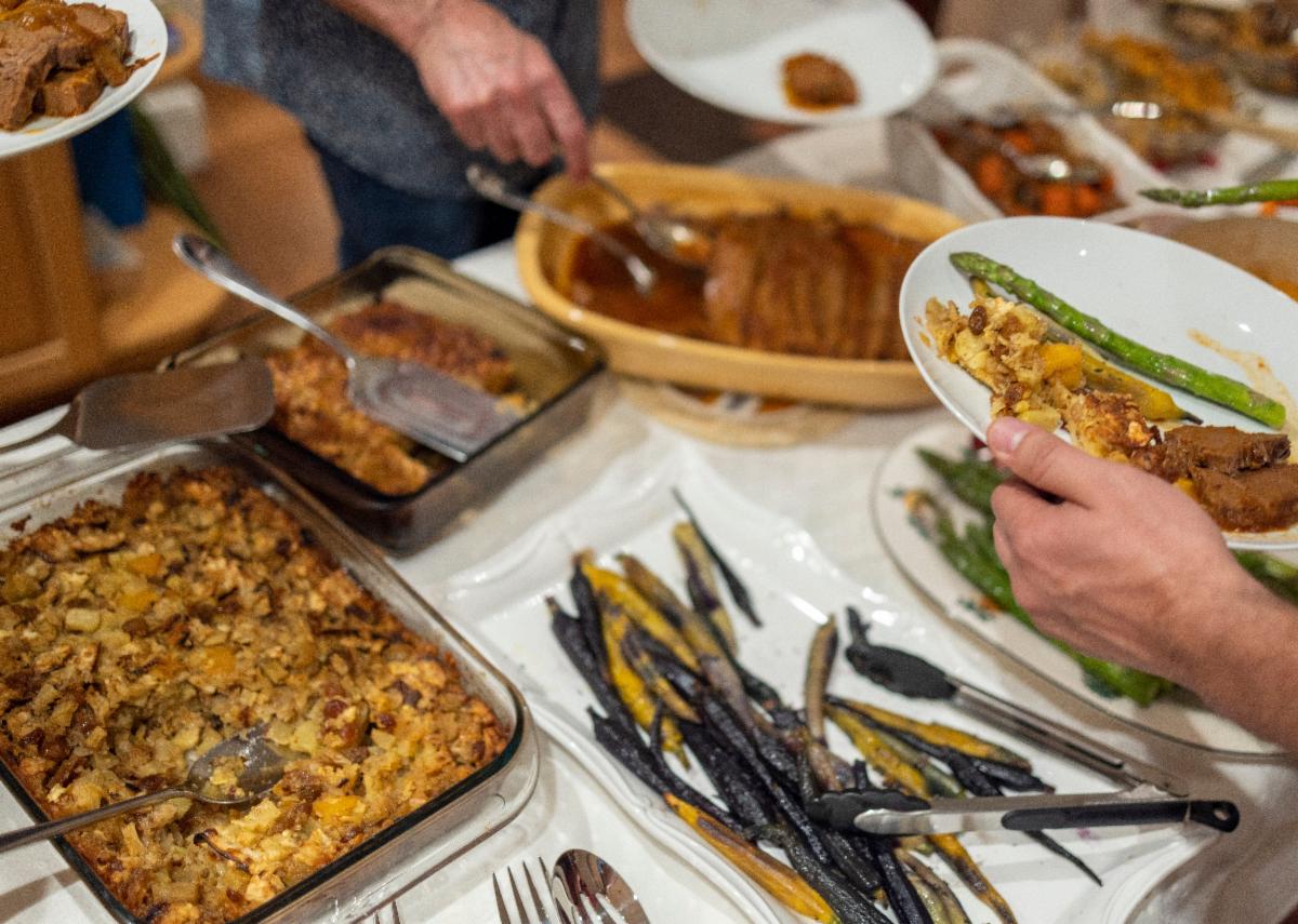 A table is coverd with many dishes of colorful food while people fill their plates