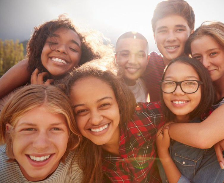A group of youth smile as they look into the camera with the sun shining behind them