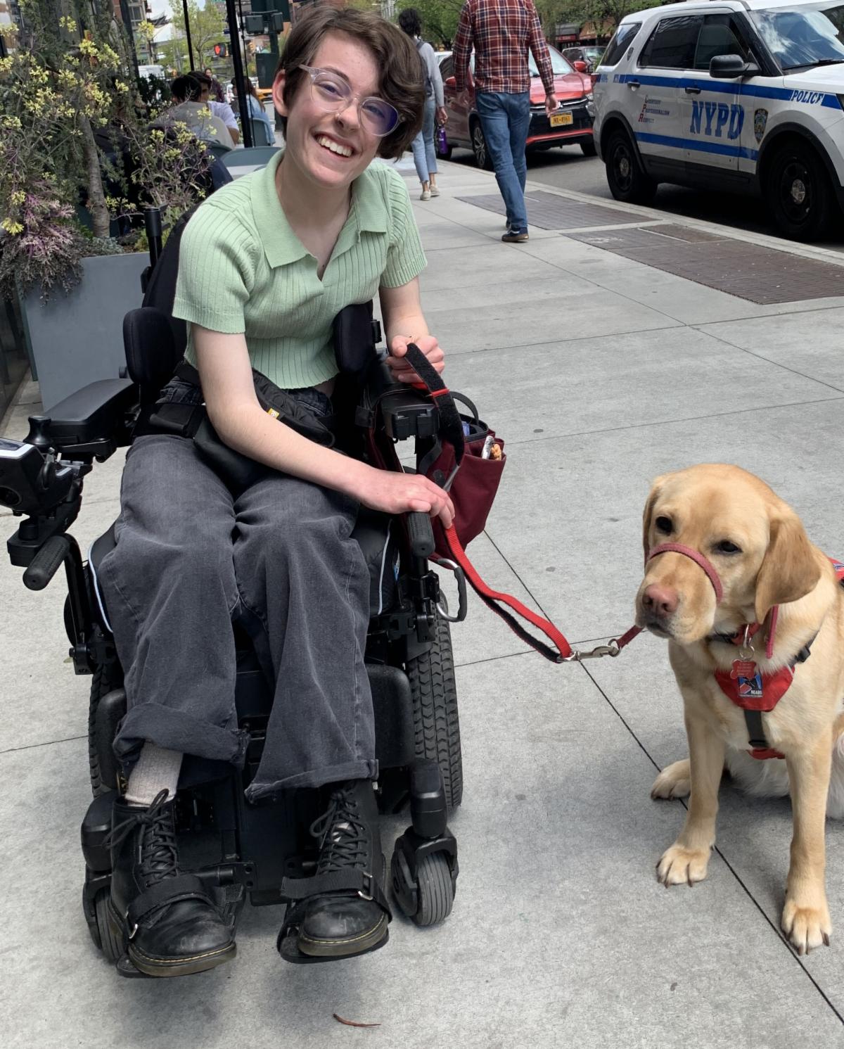 Hannah sitting in her wheelchair and smiles while she holds the leash of her dog