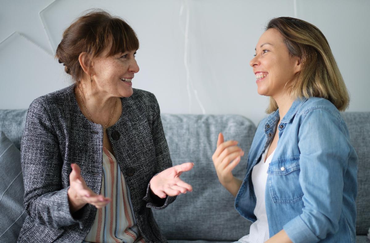 Two parents sitting on a couch and smiling while talking to each other