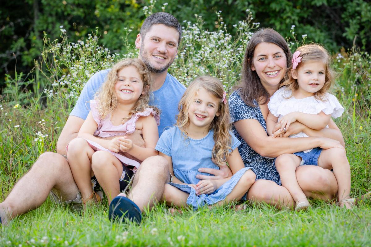 Family sitting on the lawn with trees and wildflowers behind them