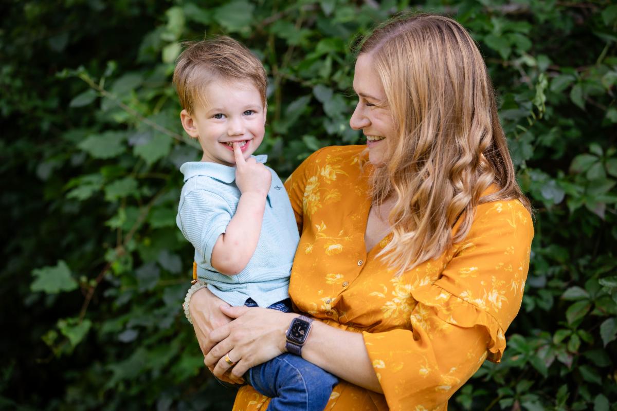 A parent in a yellow dress holds a toddler and both are smiling at each other