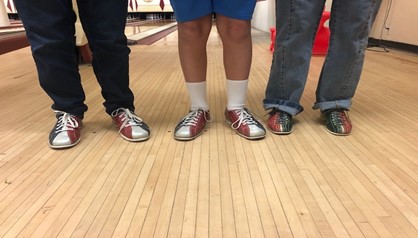 A photo of threes sets of feet wearing bowling shoes while standing on a wooden bowling lane floor