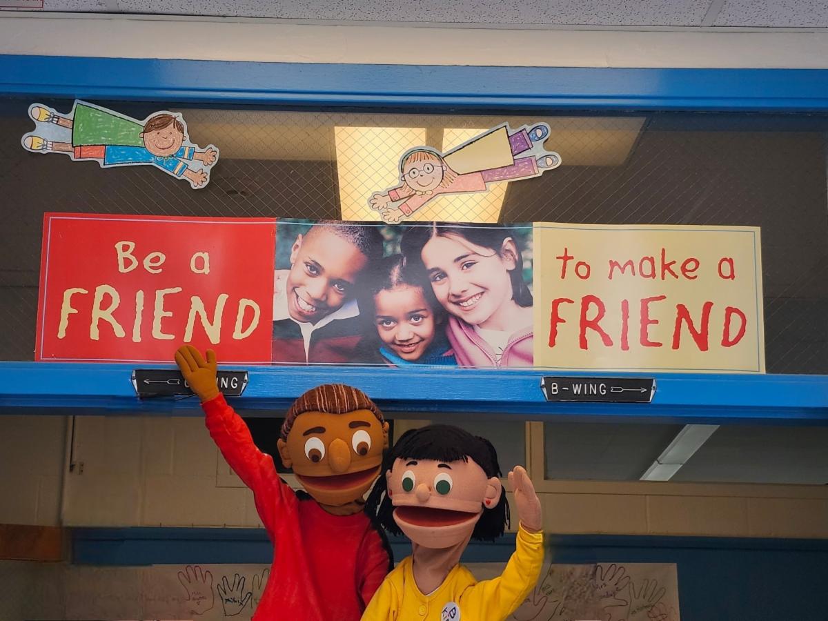 Tow puppets, one in a red shirt and one in yellow, hold up signs saying "Be A Friend" "to Make A Friend"
