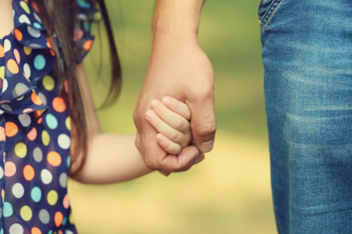 Photo of a child in polka dot dress holding the hand of a parent wearing blue jeans