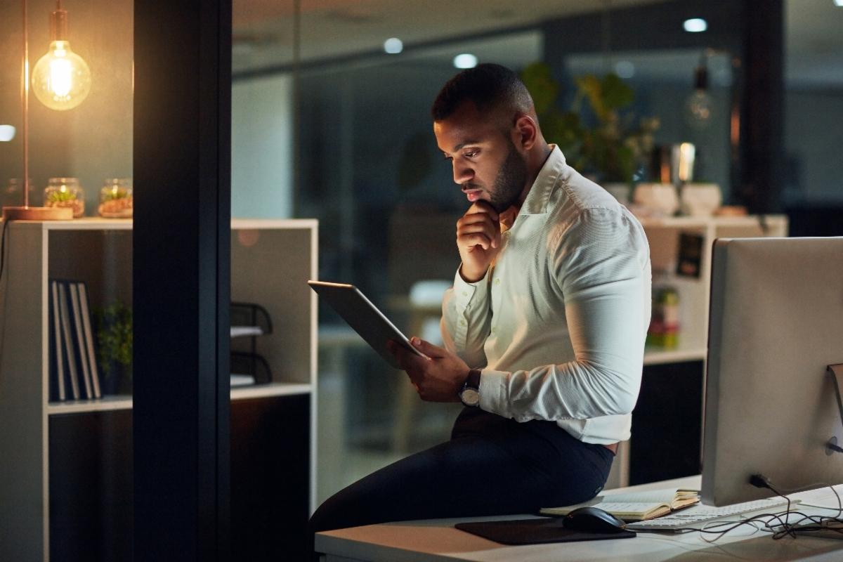 Photo of a business person looking at a table and sitting on a desk in an office at night.