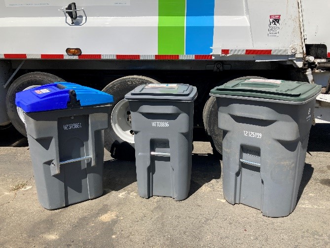 Image of a recology truck with three carts in front of it one with two blue lids for recycling one with a grey lid for trash and one with a green lid for organics
