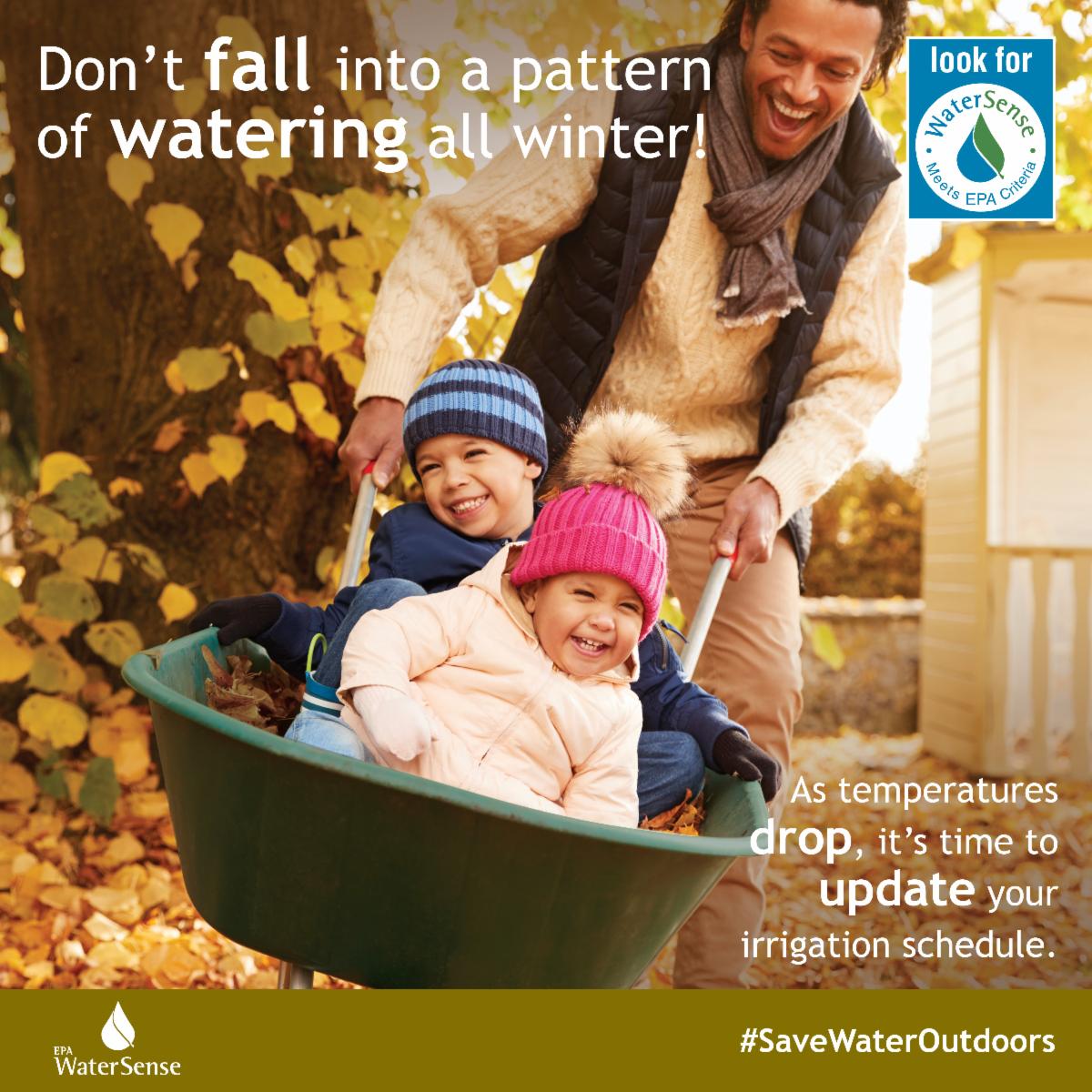 Image of a man with a grey scarf pushing a green wheel barrel with two kids inside a boy with a blue striped hat and a girl with a pink hat