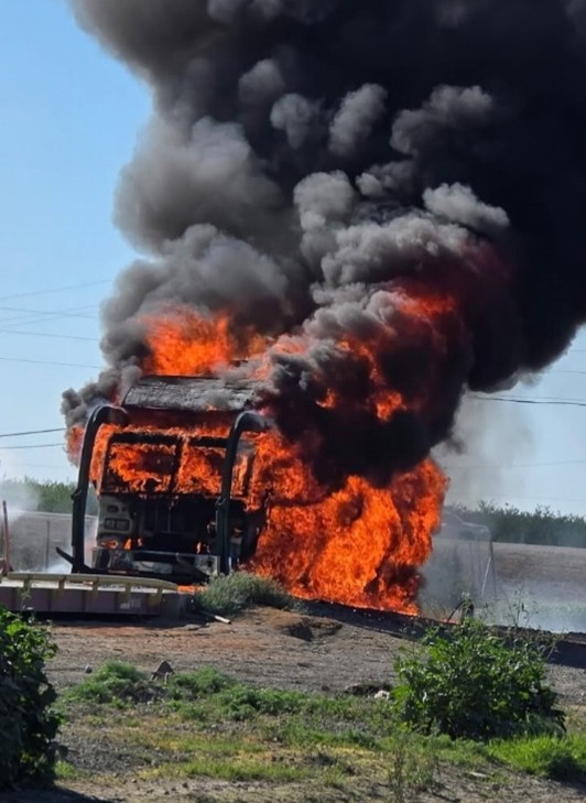 burnt out truck at a landfill with orange flames and black smoke coming from the truck frame