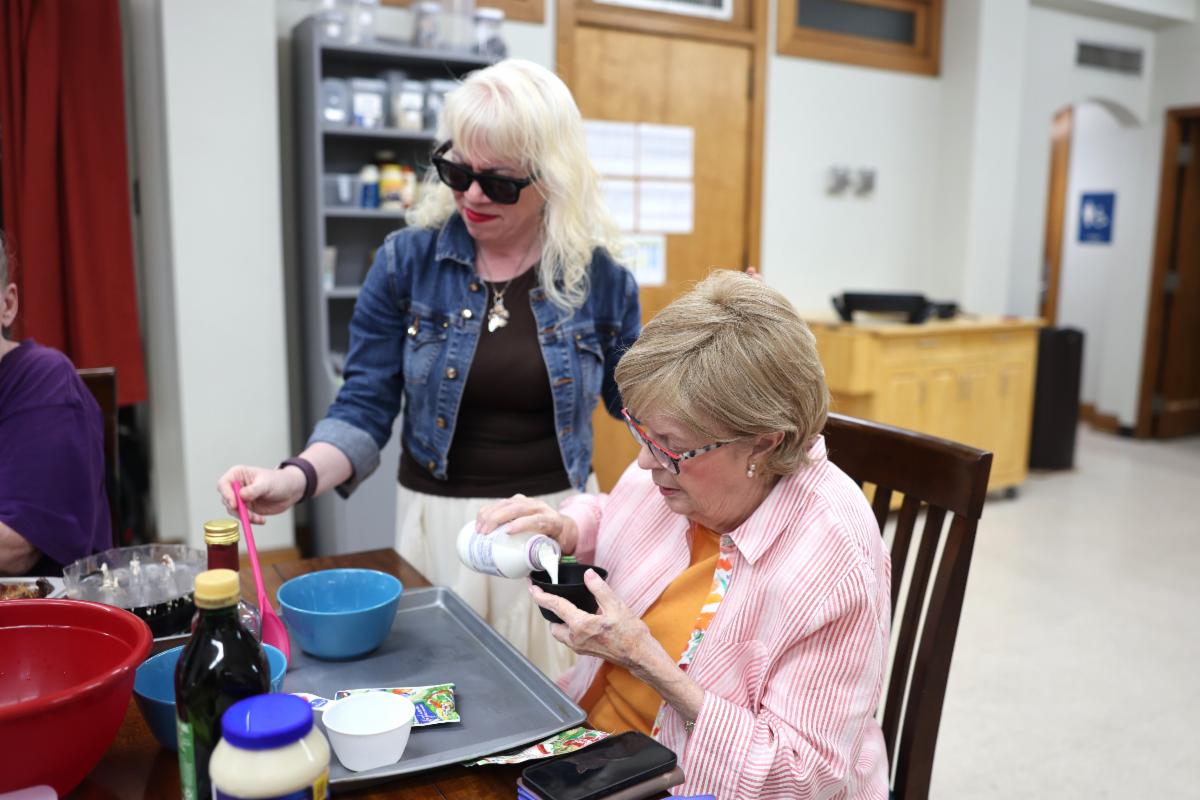 Elizabeth Swayze pours an ingredient into a measuring cup as Beckie Nollendorfs, Independent Living Skills Trainer at Vibrant Works, assists during a hands-on cooking activity.