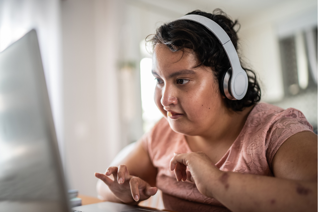A young woman wearing headphones is using a laptop, focused on the screen while typing. 