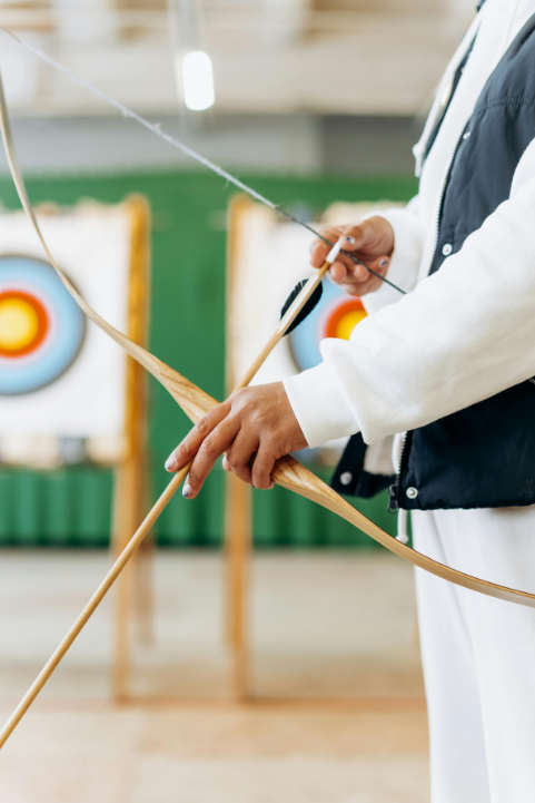 A person is setting an arrow in an archery bow. Indoor archery targets are in the background.