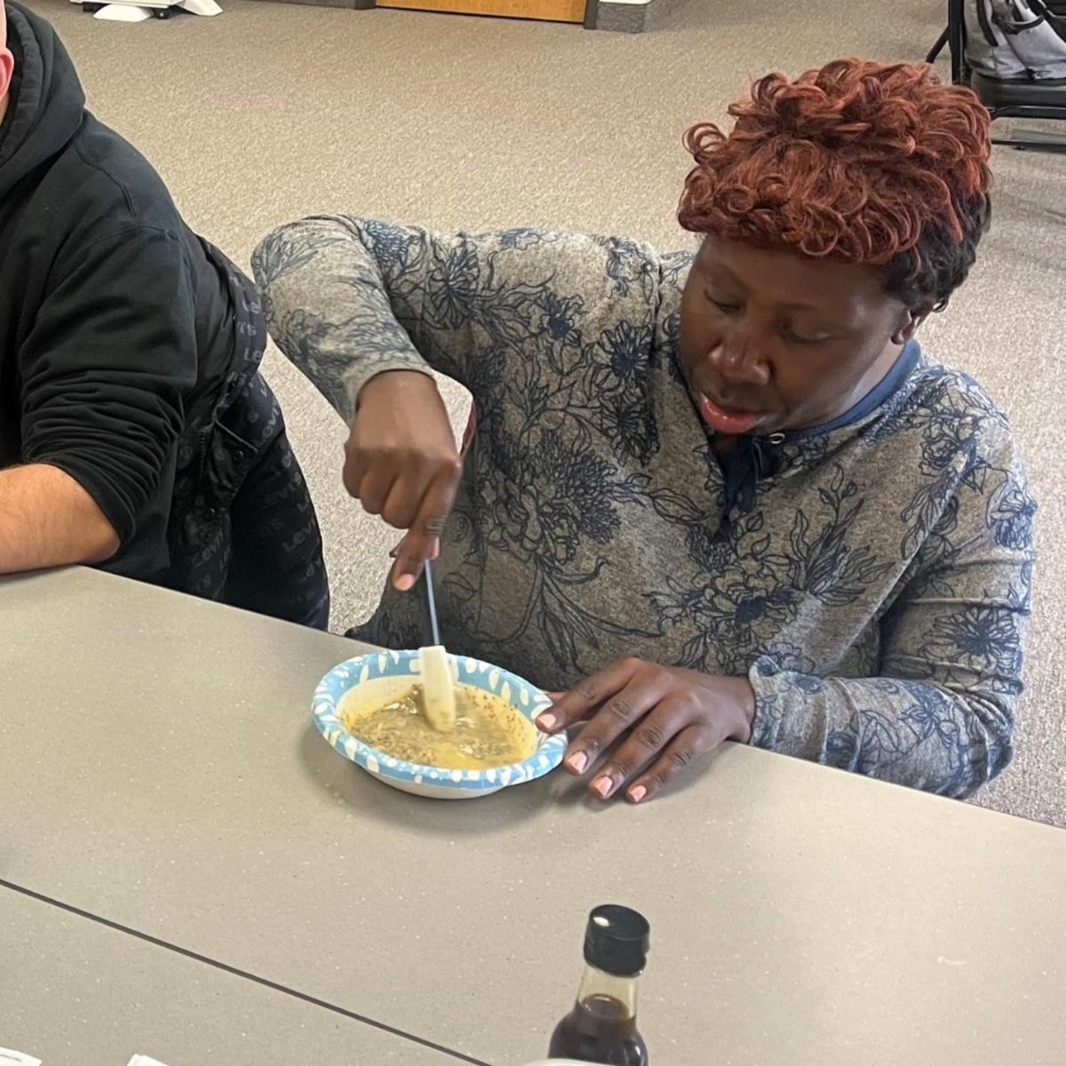 A consumer seated at a table is helping to prepare a meal during a Disability Network Eastern Michigan cooking class.