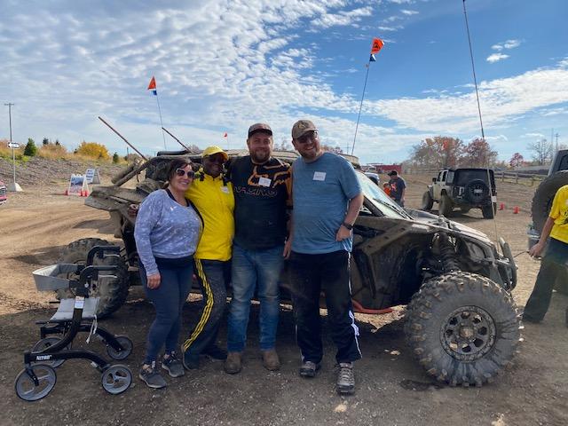 Four people stand in from of an off-road vehicle