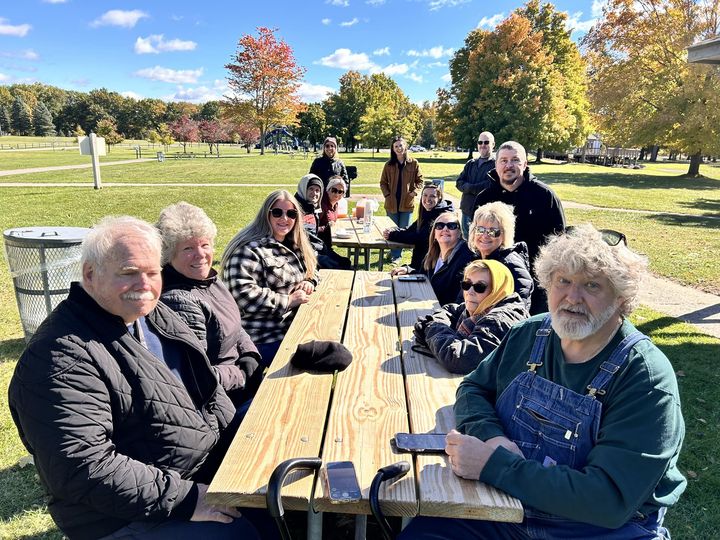 14 stroke support group members are gathered around picnic tables in a park