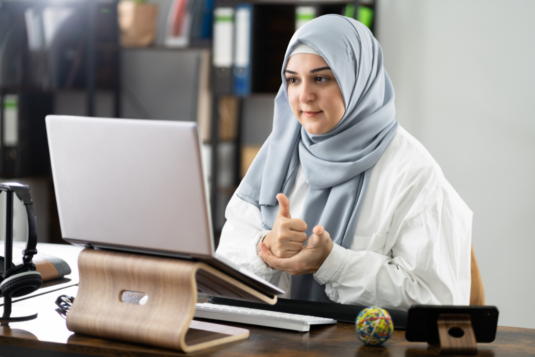 A woman wearing a head scarf is practicing ASL in a video call.