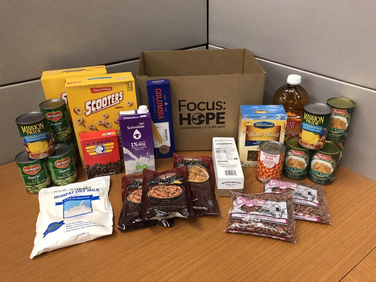 A cardboard box labeled with the Focus Hope logo is surrounded by shelf-stable food.