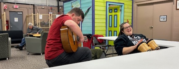 A woman is playing hand drums, accompanied by a man playing a guitar.
