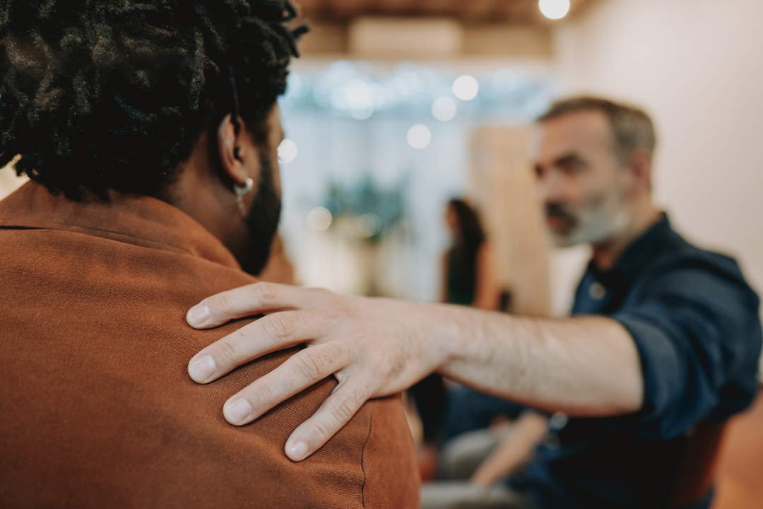 A man provides a reassuring pat on the shoulder to another support group member.