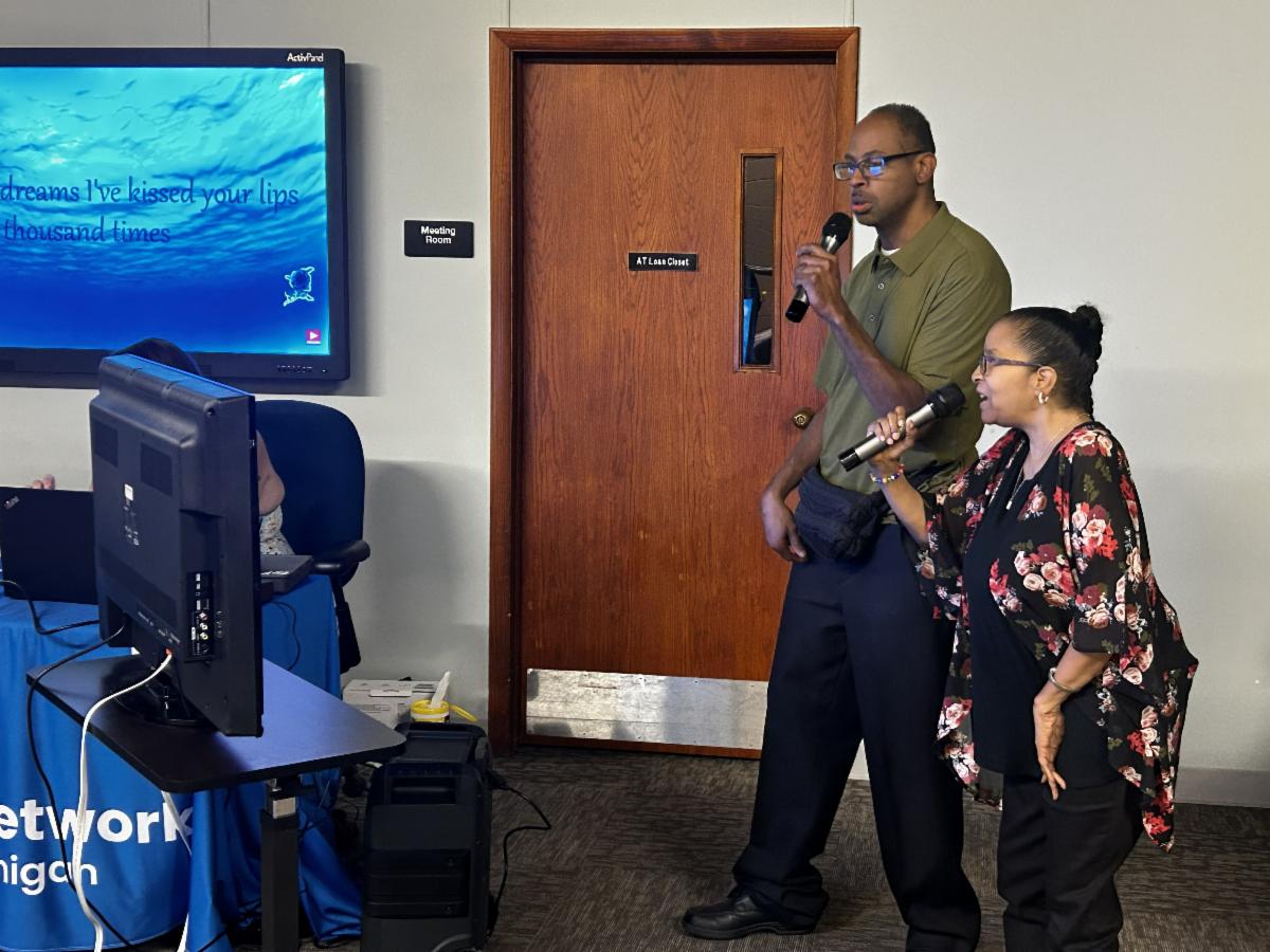 Two people are singing karaoke together. They are reading the lyrics from a monitor.
