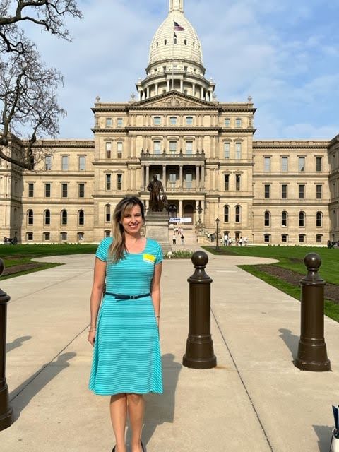 Lauren Baker, Public Policy & Outreach Specialist at Disability Network Eastern Michigan stands in front of the State of Michigan capitol at legislative day.