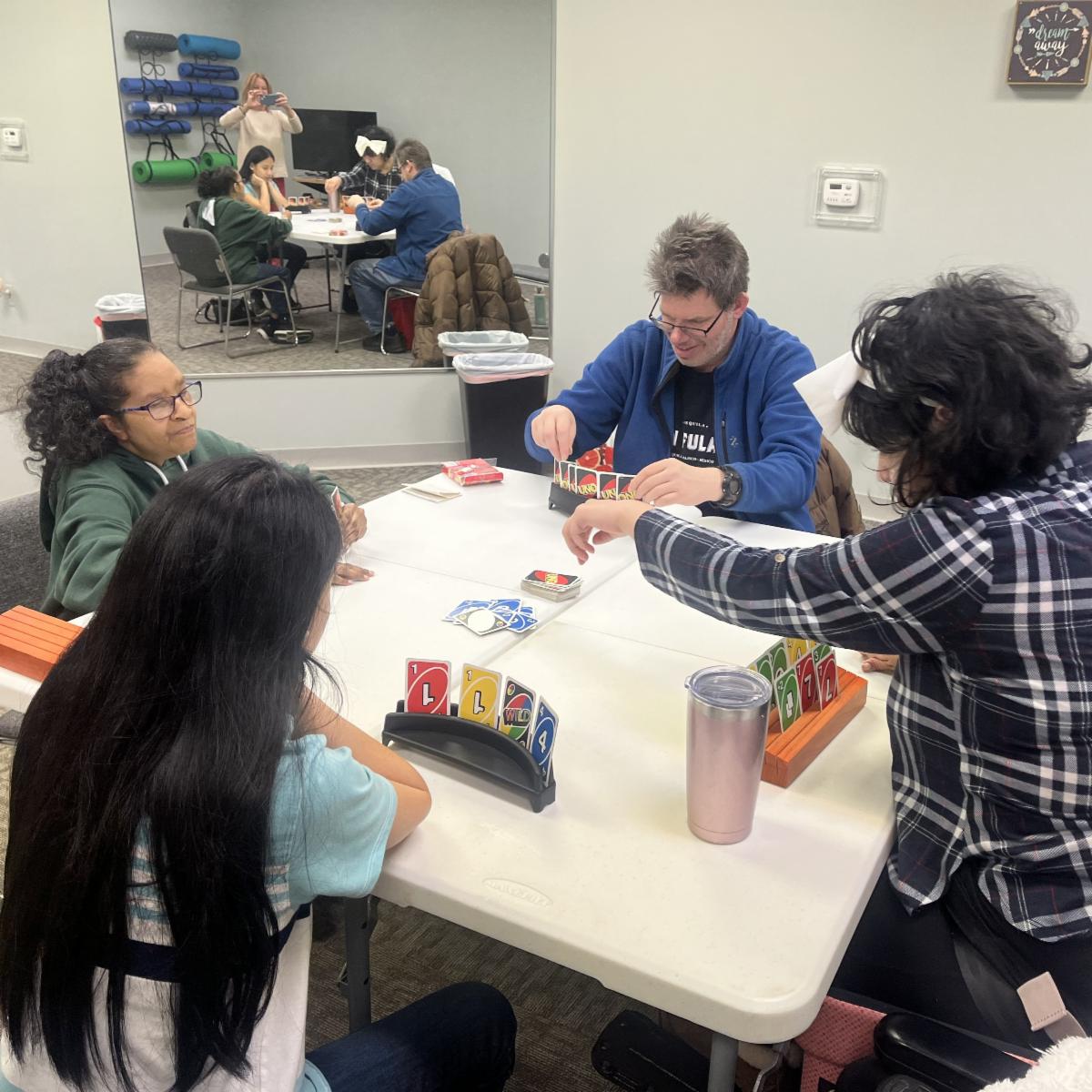 Four people are seated around a table playing UNO.