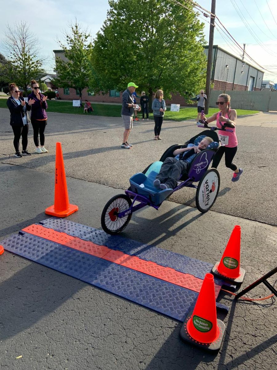 A woman pushing a young man in a running chair approaches the finish line of a 5K race.